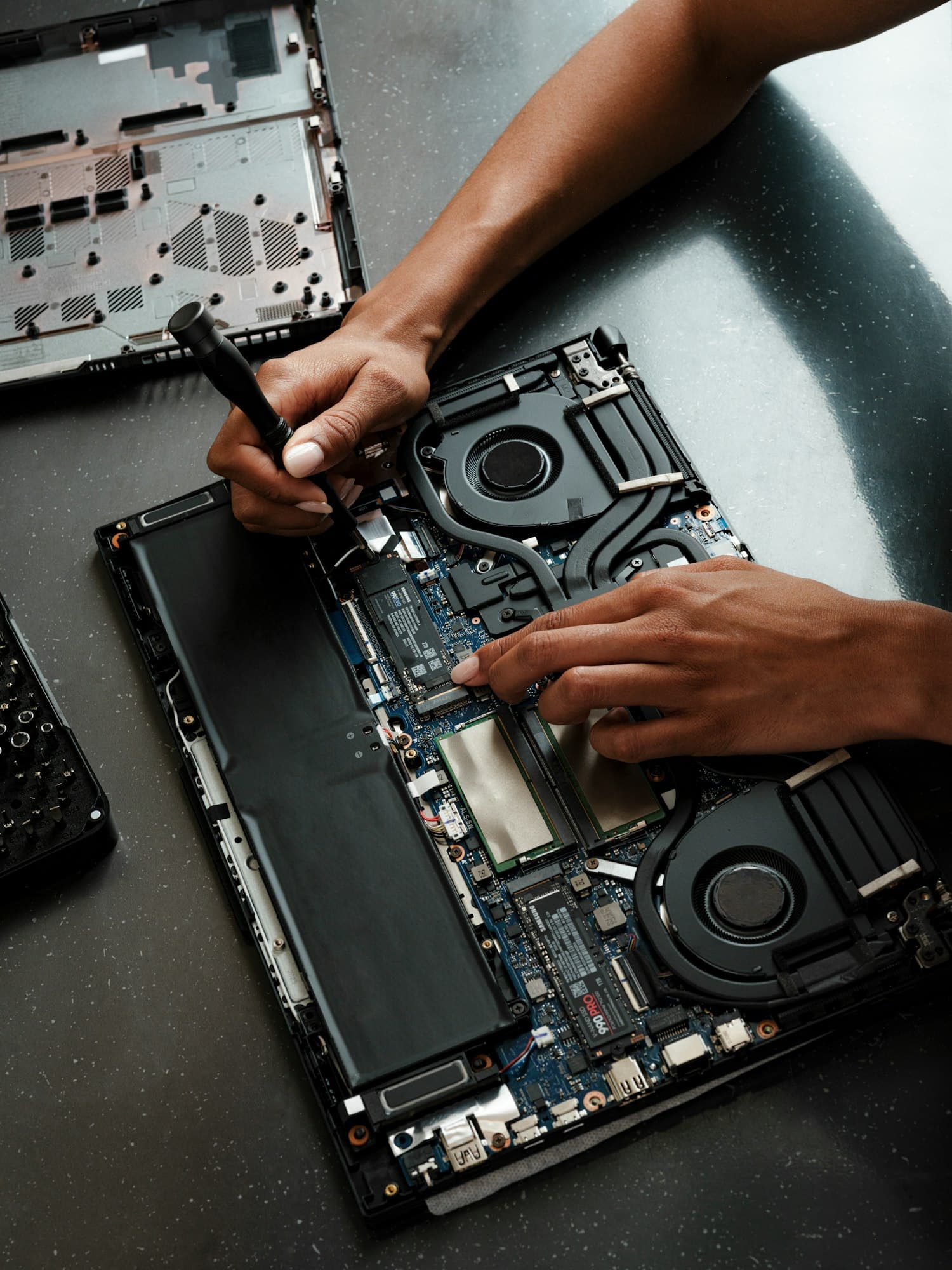 A technician opens a laptop at the bench, screwdriver in hand, mid-repair